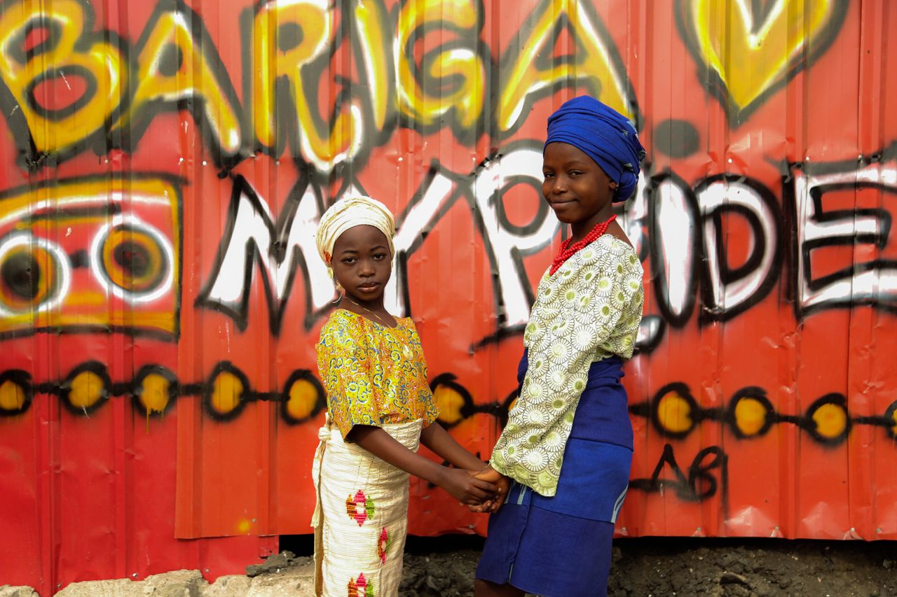 Home Two children hold hands against a vibrant graffiti wall in Bariga, showcasing cultural pride.
