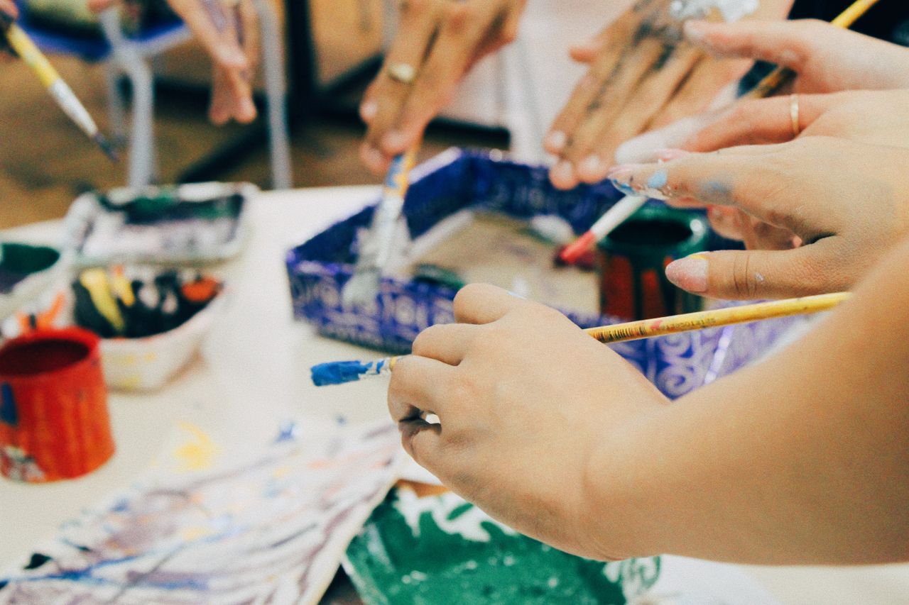 Home Group of hands holding paintbrushes in a vibrant art workshop, encouraging creativity.