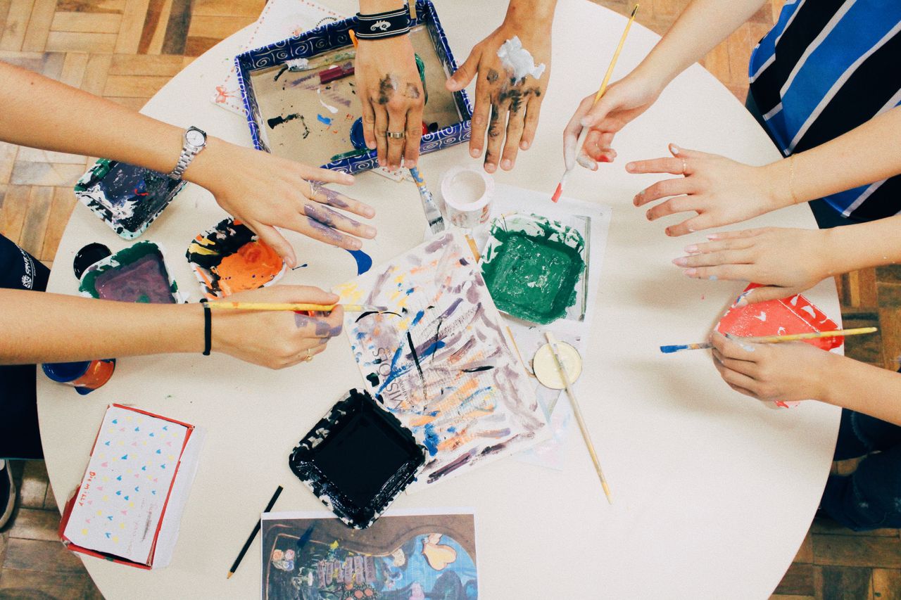 Home A group of people engaged in a creative painting session using mixed media on a round table.