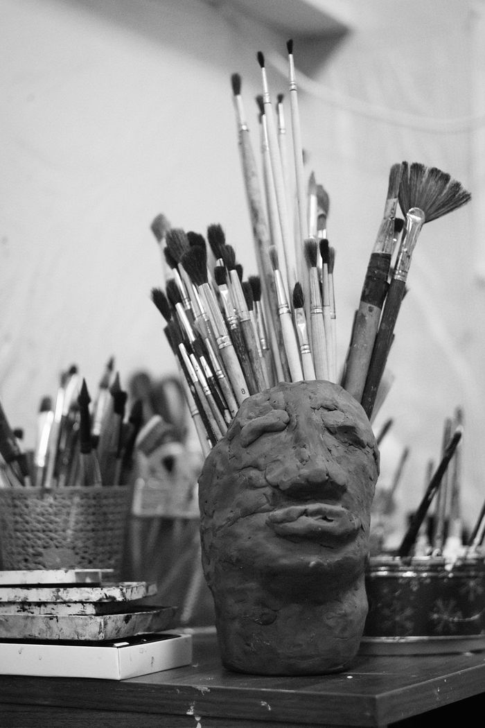 Home A creative black and white image of a sculpture holding paintbrushes in an artistic studio setting.