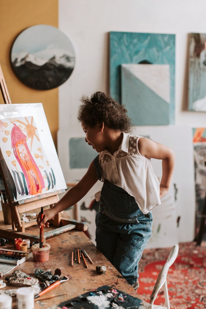 Home A young girl joyfully painting at an easel in an art studio.